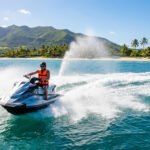 Un homme en gilet de sauvetage orange sur un jet ski argenté fendant les eaux turquoise de Maurice, avec plage et montagnes en fond.